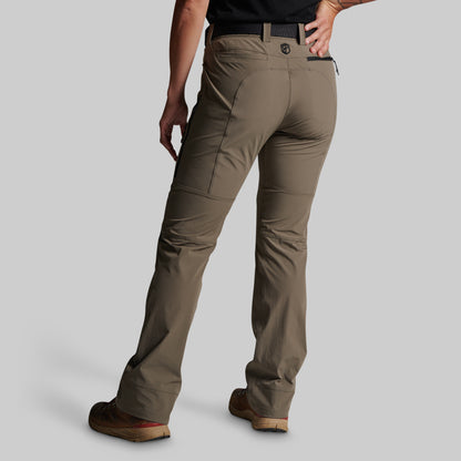 A person shown from the back wearing grey cargo pants, a black shirt, and brown shoes against a light gray studio background.