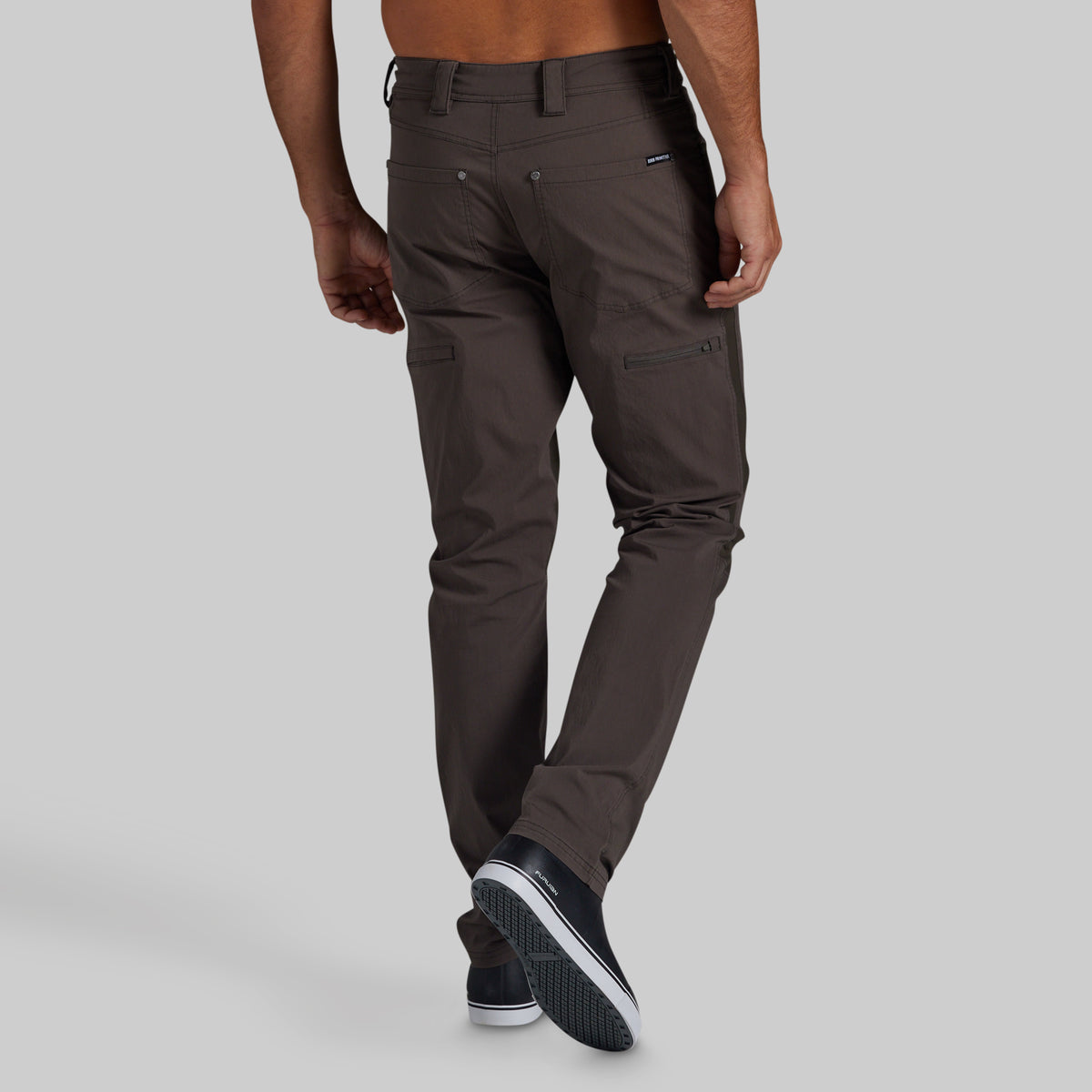 A man wearing dark brown slim-fit cargo pants, shown from the back and side against a solid light gray background.