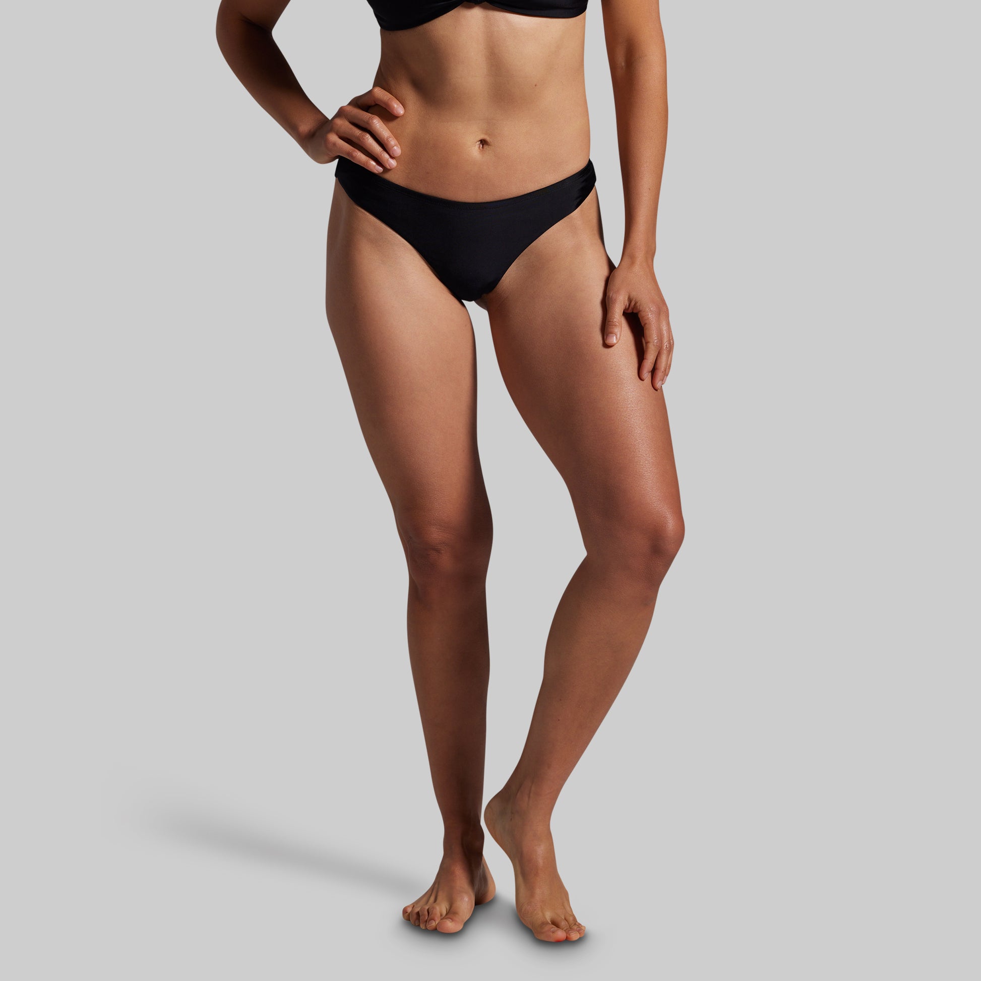 Person wearing black bikini bottoms on a gray background