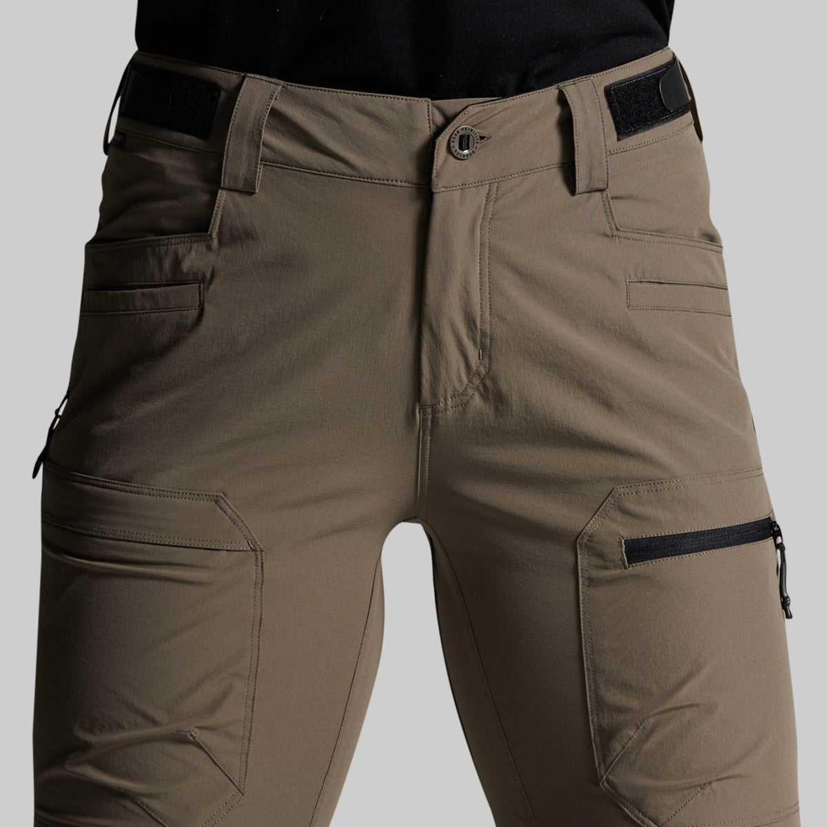 Close-up of a person wearing cargo-style pants in a storm grey color, with black belt and zipper accents, against a light gray studio background.
