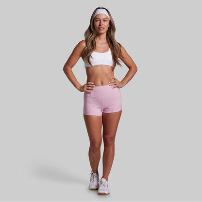 Woman wearing a white sports bra and pink shorts on a gray background