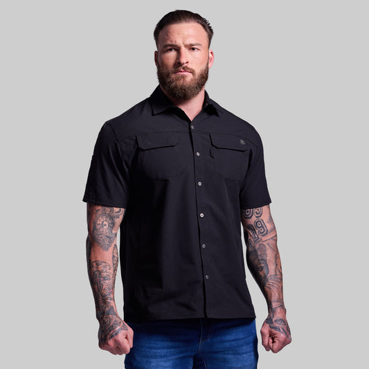 Man wearing a black collared short-sleeve shirt against a gray background