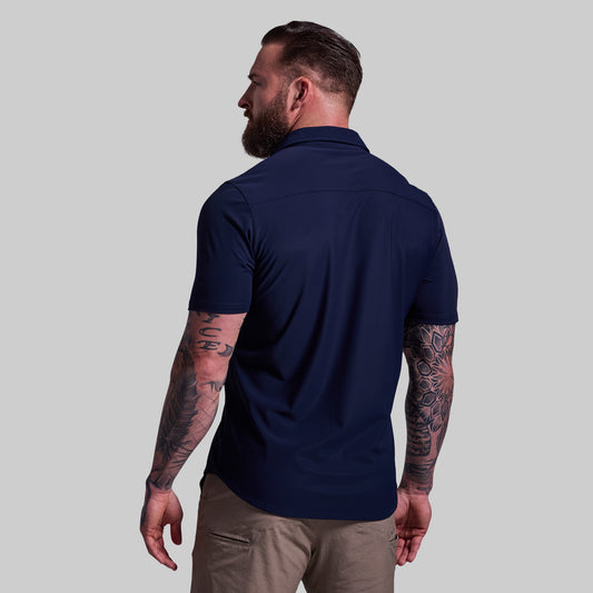 Man wearing a navy blue shirt and beige pants against a gray background