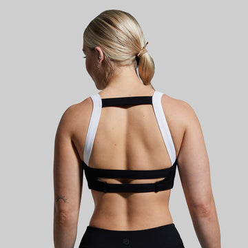 Person wearing a black sports bra with white straps on a plain background