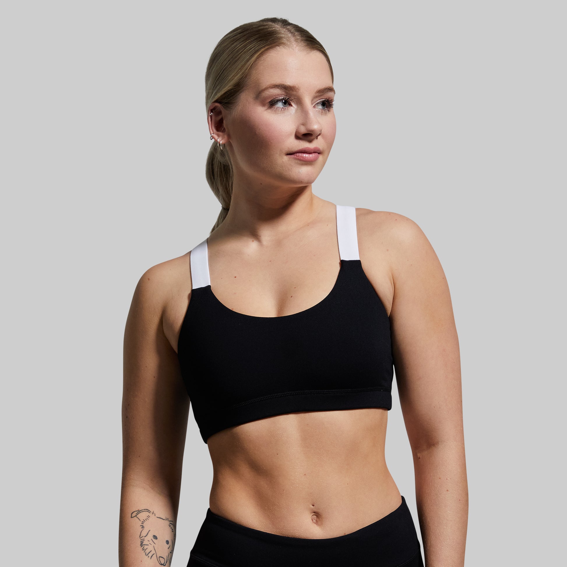 Woman wearing a black sports bra with white straps on a plain background