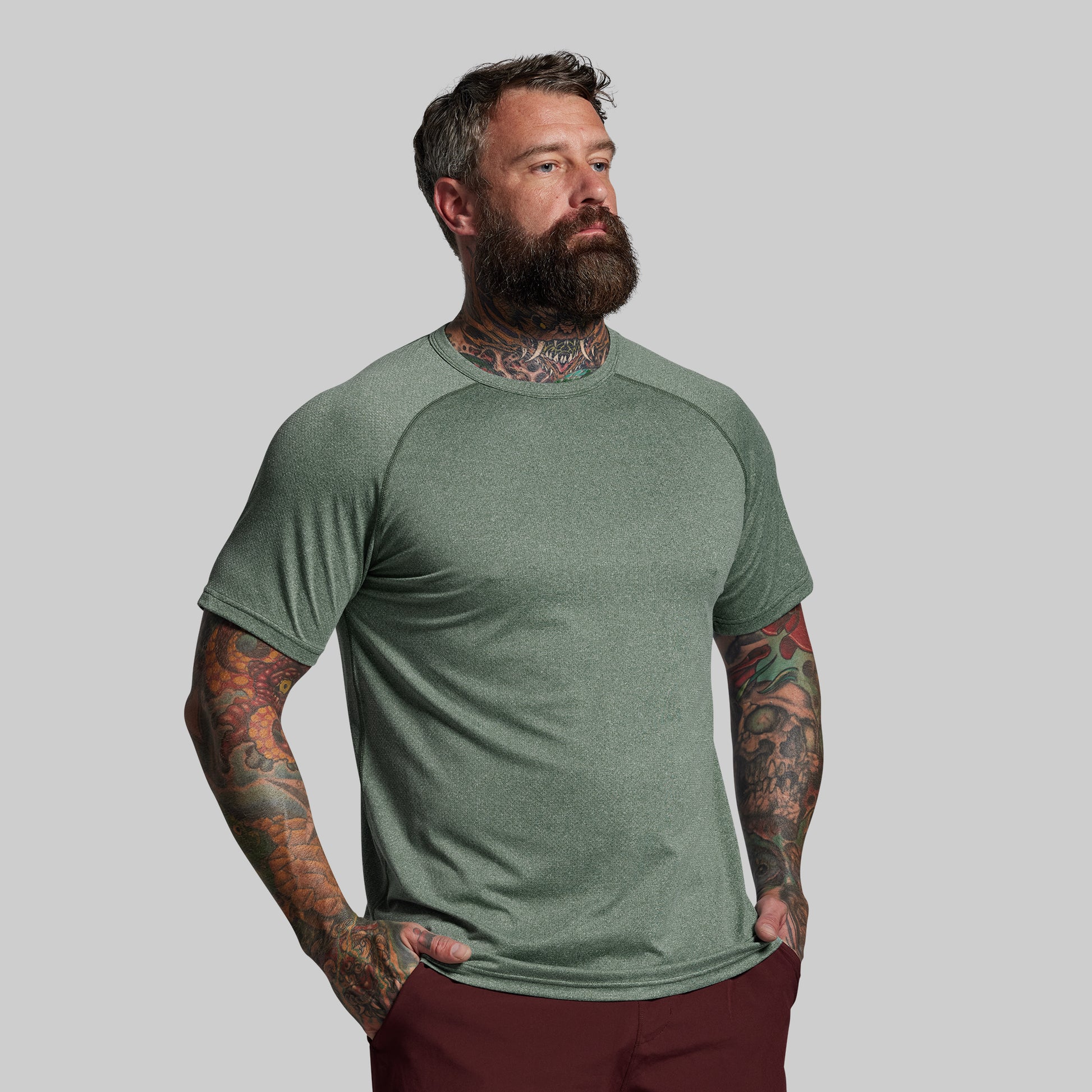 Man wearing a green t-shirt with tattoos on his arms against a gray background
