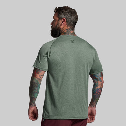 Man wearing a green t-shirt with a small logo on the back against a gray background