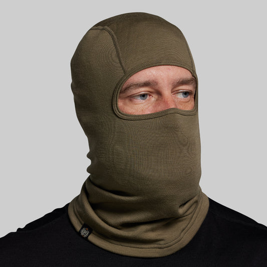 Person wearing a green balaclava against a gray background