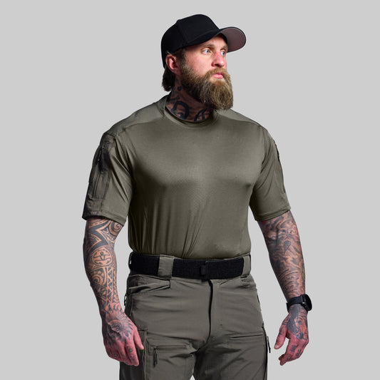 Man wearing an olive green tactical outfit with a black cap on a gray background