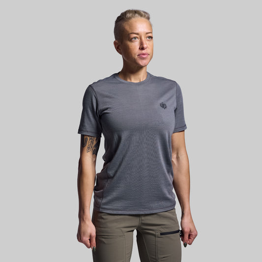 Person wearing a gray t-shirt with a small logo on a plain background