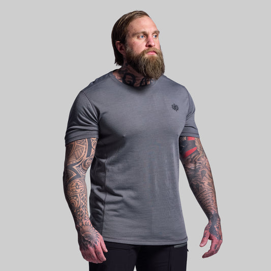 Man wearing a gray t-shirt with tattoos on arms against a plain background