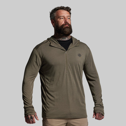 Man wearing a green hooded base layer on a gray background