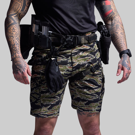 Person wearing camouflage shorts and tactical gear on a gray background
