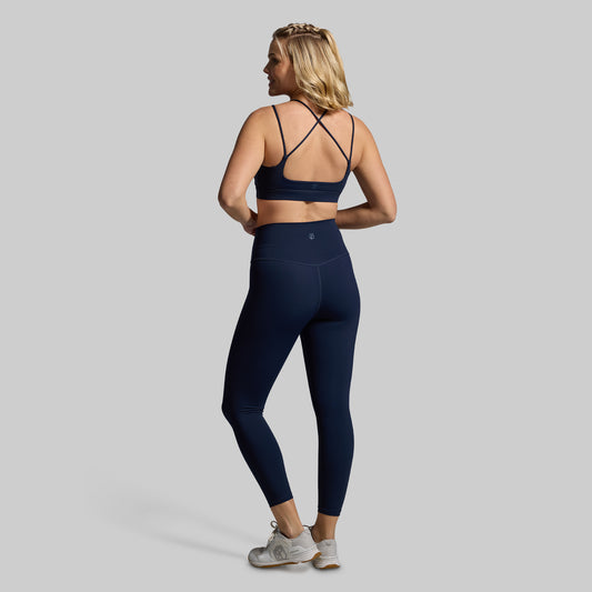 Woman wearing a navy blue sports bra and leggings set on a gray background