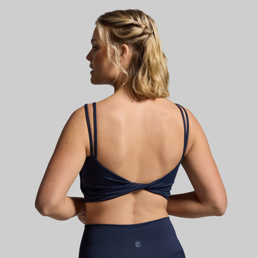 A navy sports bra with a unique twisted back design, viewed from the back.