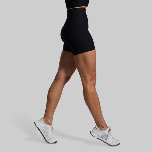A model wearing high-waisted black shorts with a ribbed texture, paired with white sneakers.