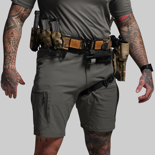 Person wearing tactical shorts and belt with multiple pouches on a gray background