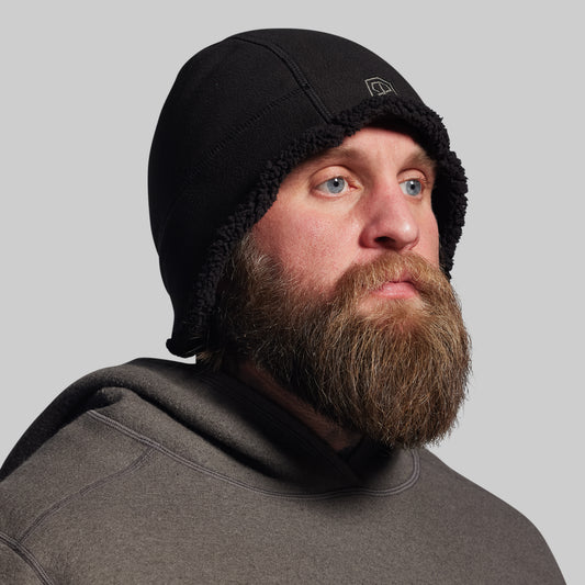Man wearing a black beanie and gray hoodie against a gray background