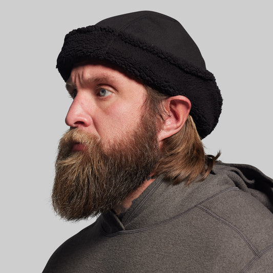 Man with a beard wearing a black beanie against a gray background