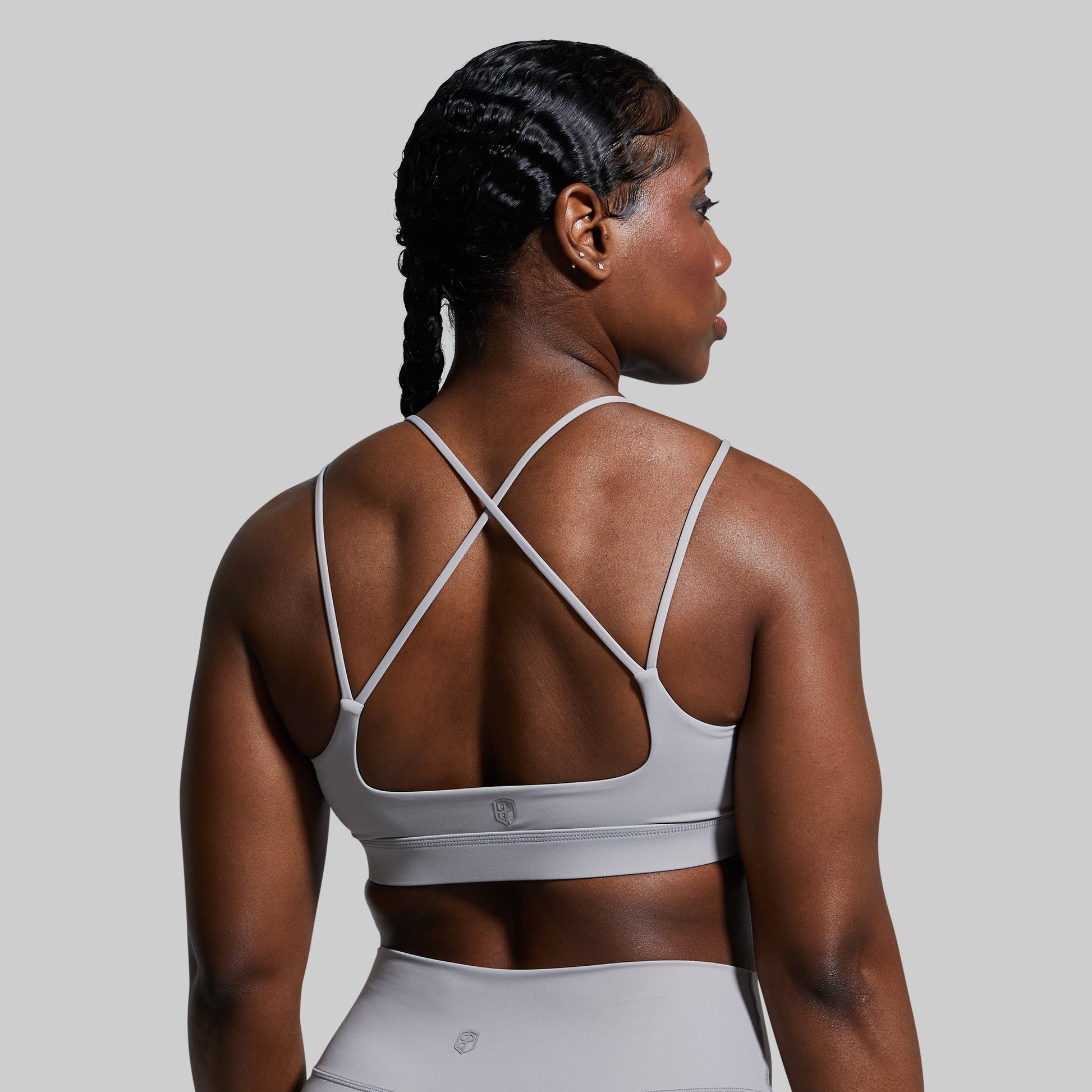 Woman wearing a gray sports bra and leggings on a plain background