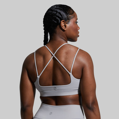 Woman wearing a gray sports bra and leggings on a plain background
