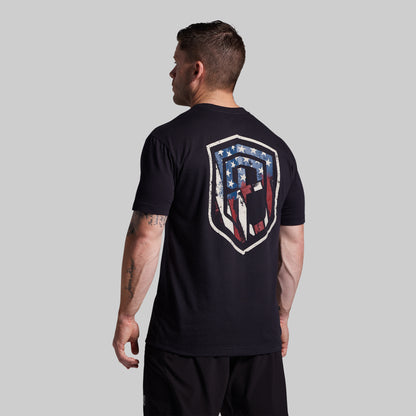 Man wearing a black t-shirt with a logo on the back against a gray background