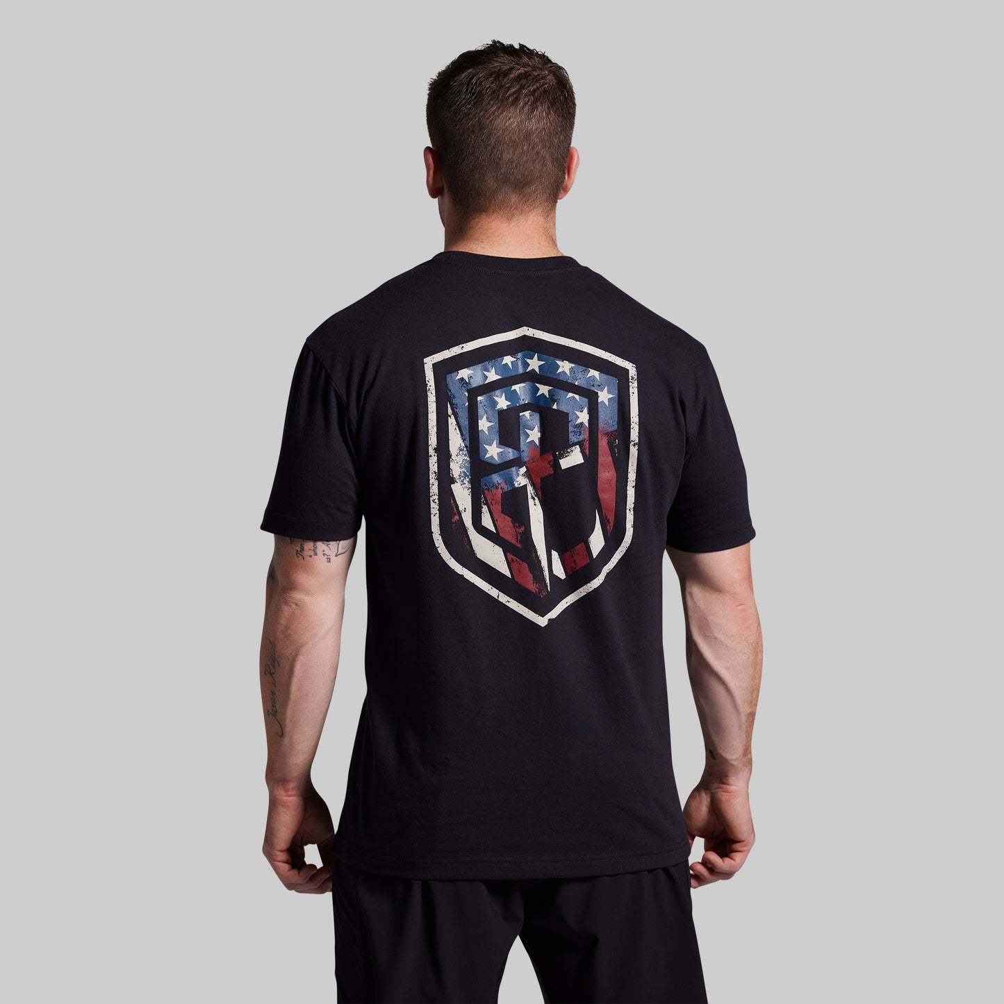 Man wearing a black t-shirt with a shield design on the back against a gray background