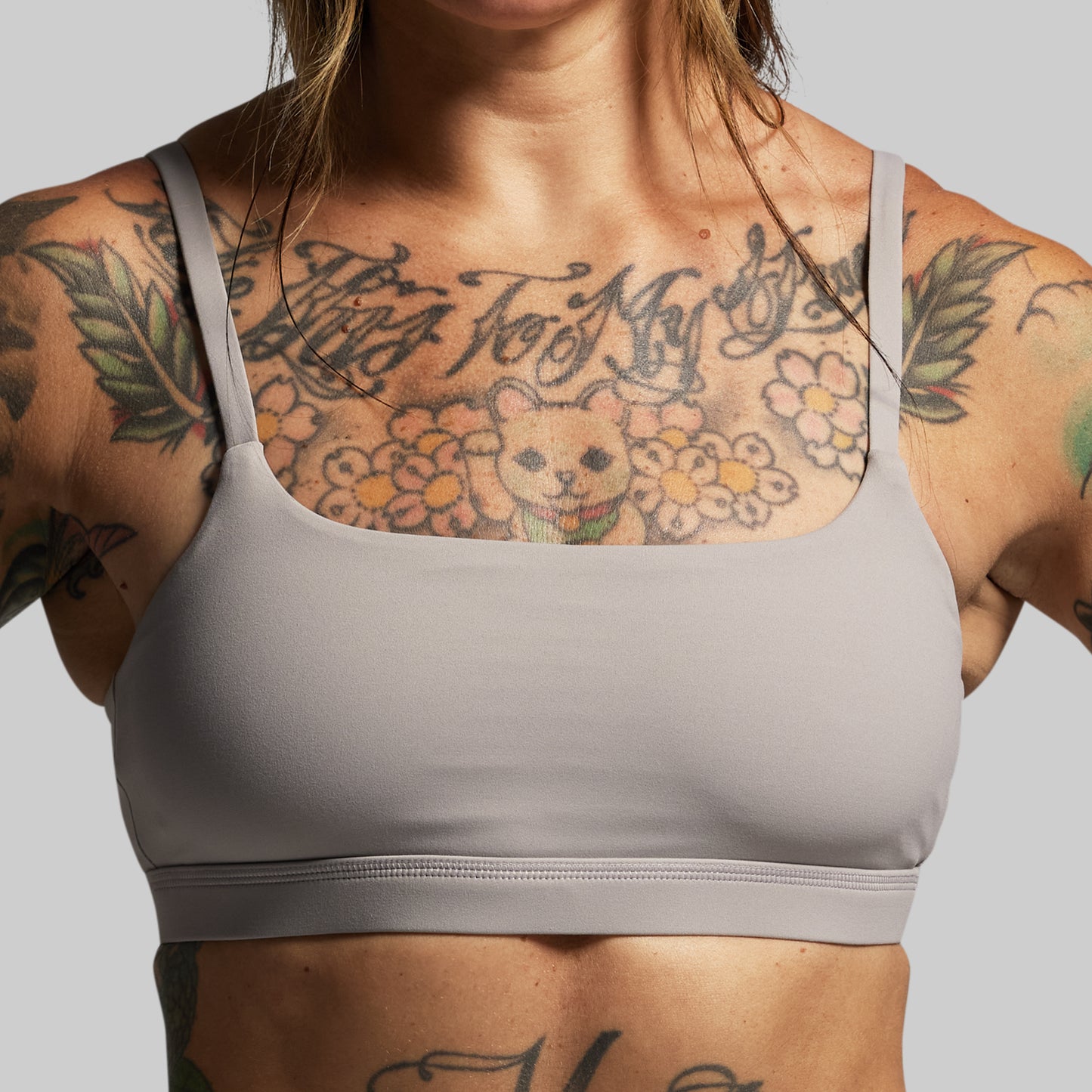 Person wearing a gray sports bra with tattoos on a plain background