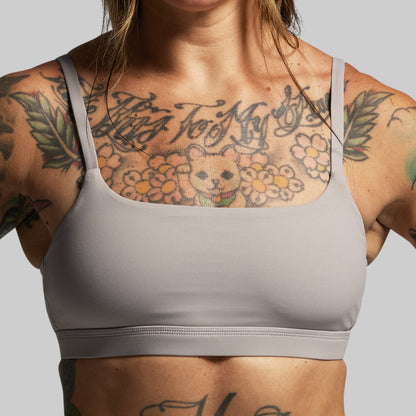 Person wearing a gray sports bra with tattoos on a plain background