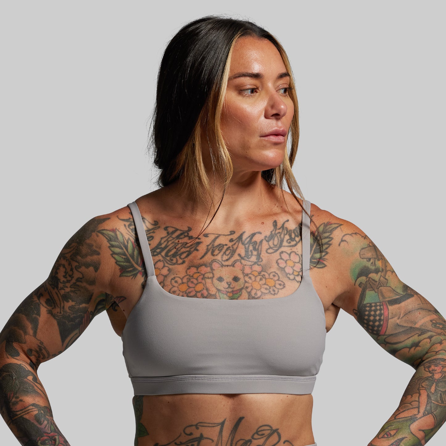 Woman wearing a gray sports bra with tattoos on a plain background