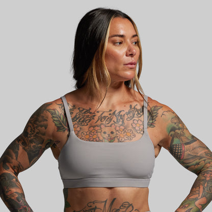 Woman wearing a gray sports bra with tattoos on a plain background