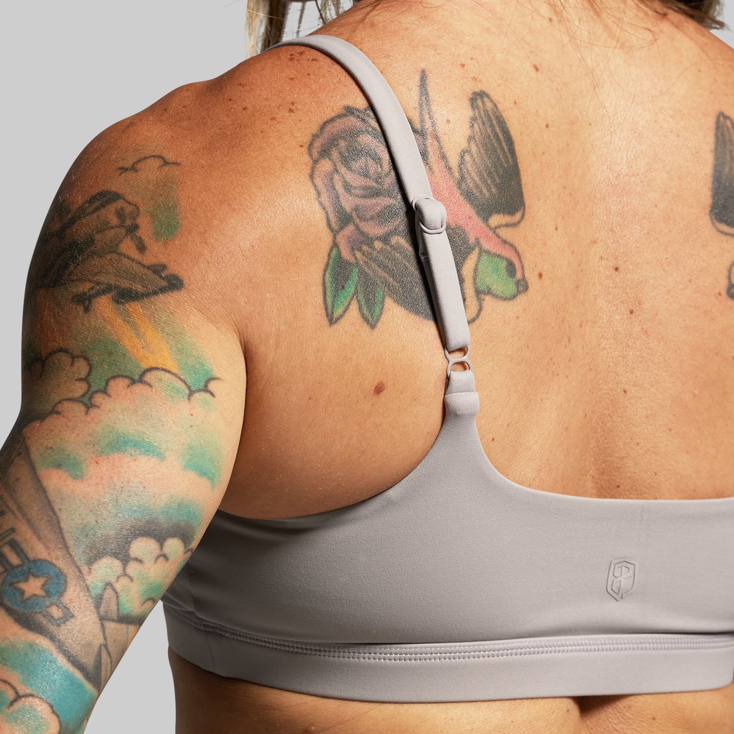 Person wearing a gray sports bra with tattoos on arms and back