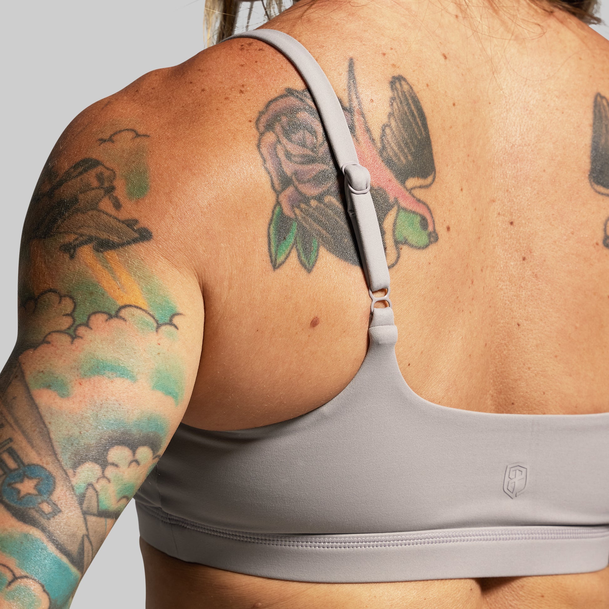 Person wearing a gray sports bra with tattoos on arms and back