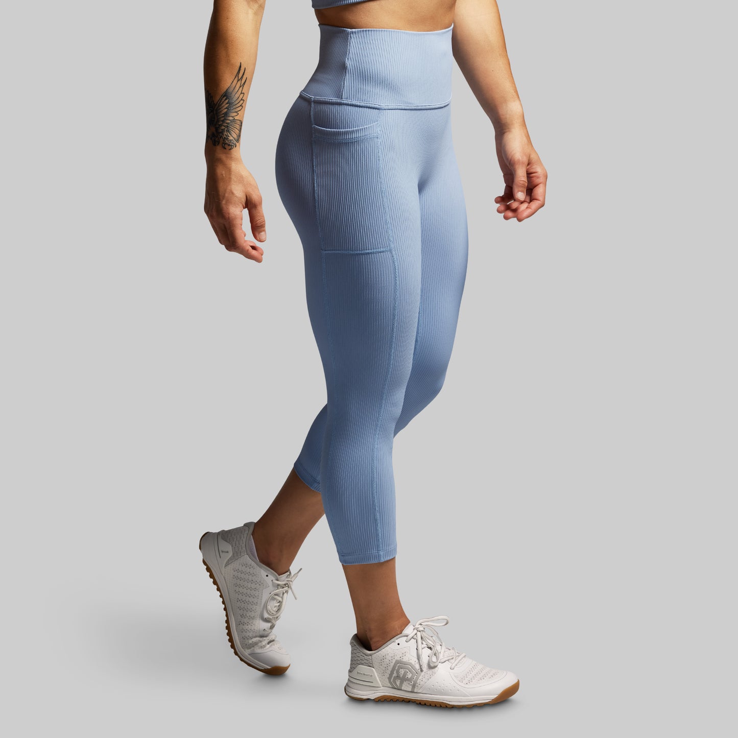 Person wearing light blue leggings and white sneakers on a gray background