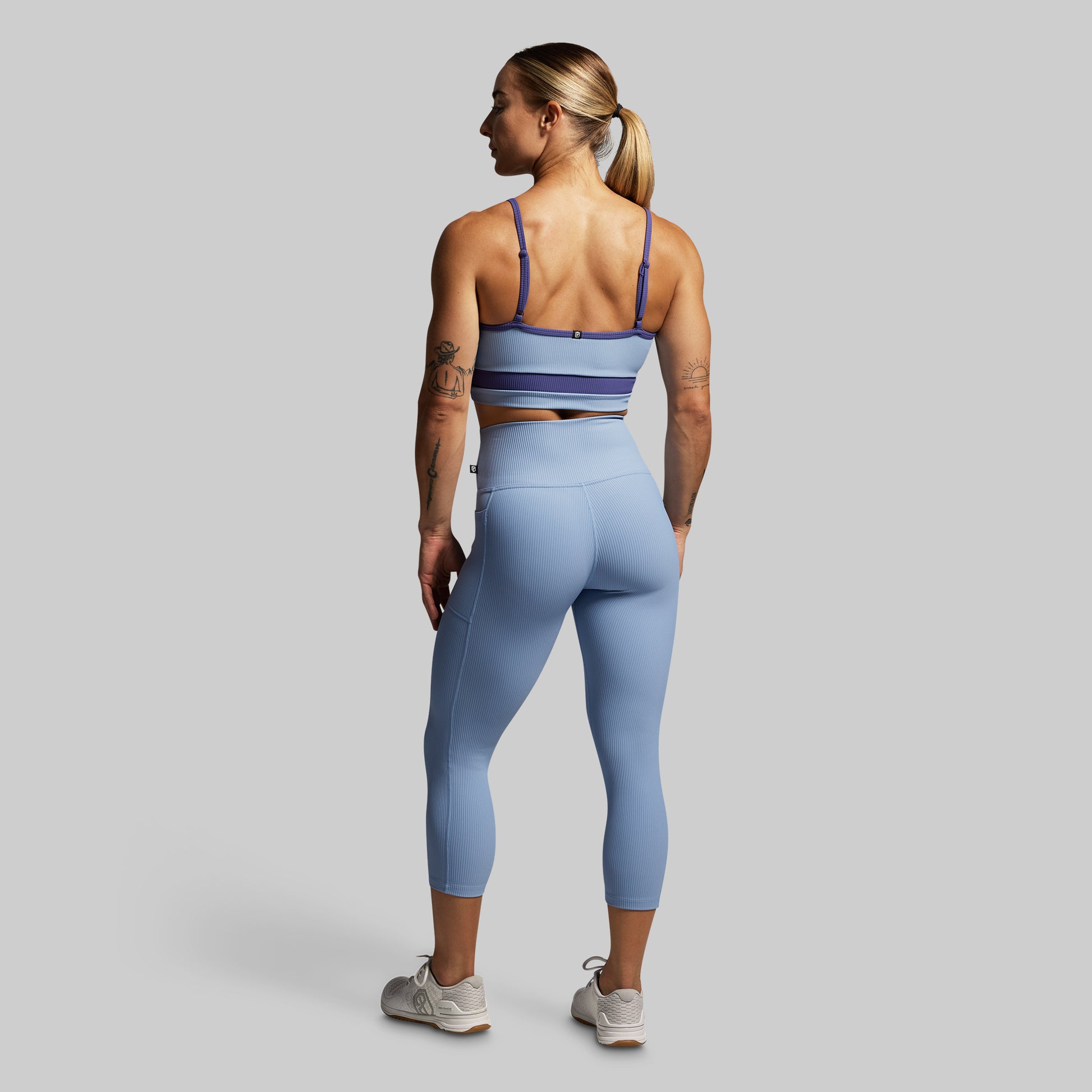 Woman wearing a blue sports bra and leggings on a gray background