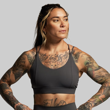 Woman wearing a grey sports bra and leggings with tattoos on a gray background