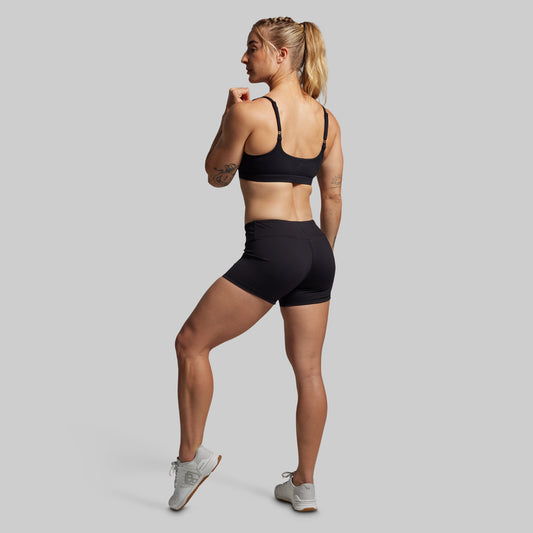 Woman wearing a black sports bra and shorts on a gray background