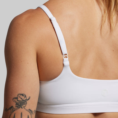 White sports bra worn by a person with a tattooed arm on a neutral background.