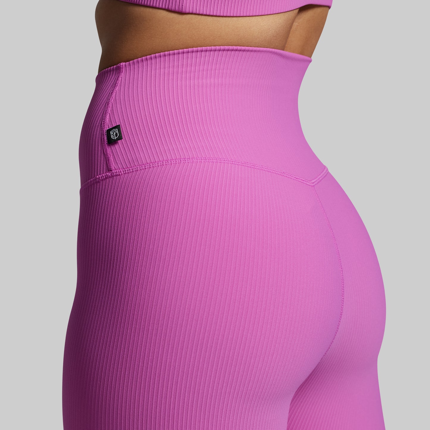 Close-up of pink ribbed leggings with a brand logo on a gray background
