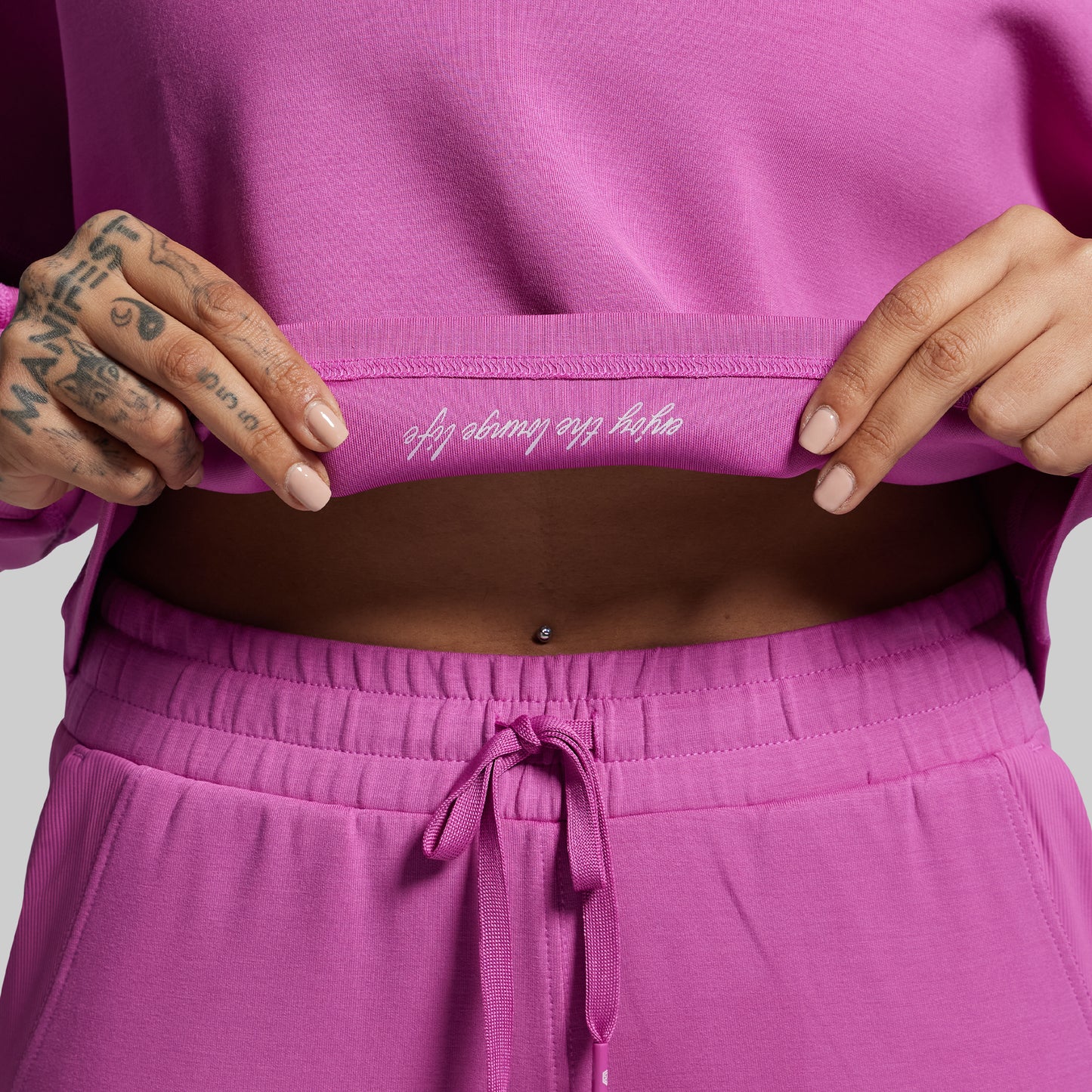 Person wearing a pink outfit with text on the waistband against a light gray background