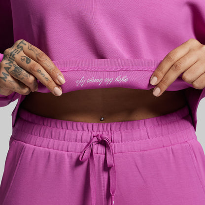 Person wearing a pink outfit with text on the waistband against a light gray background