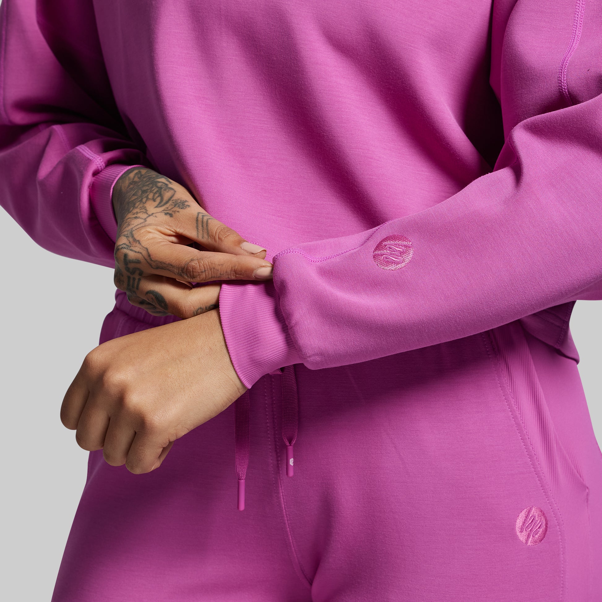 Close-up of a person wearing a pink sweatshirt with brand logos on a light gray background
