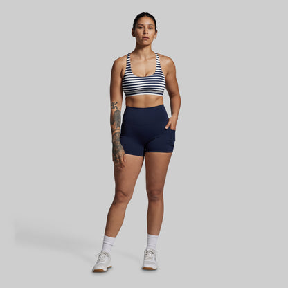 Woman wearing a striped sports bra and navy shorts on a gray background