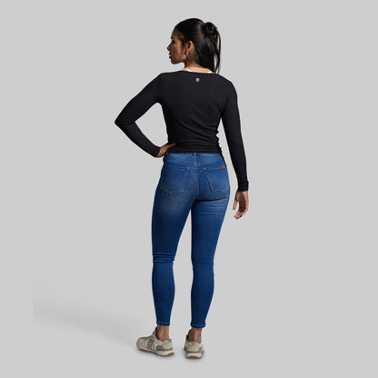 Person wearing blue jeans and a black long-sleeve shirt on a gray background