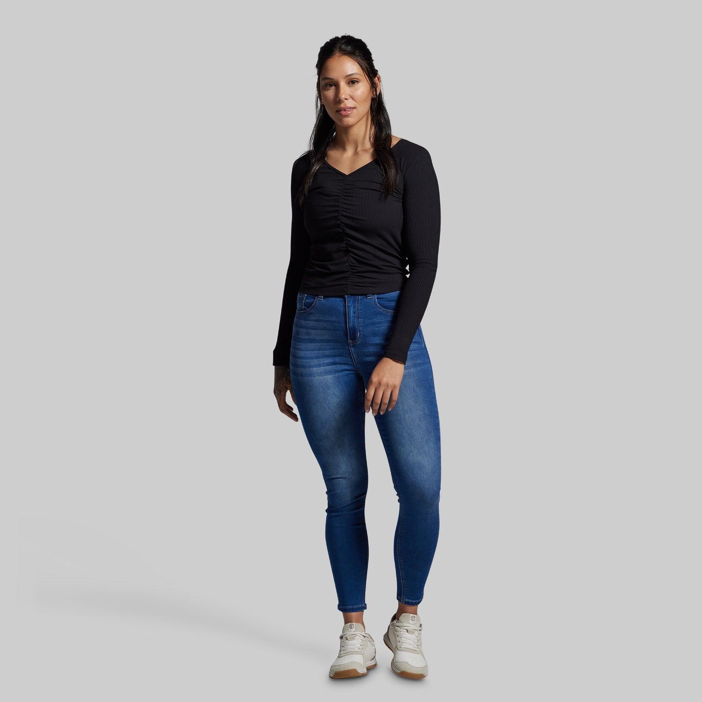 Woman wearing blue jeans and a black long-sleeve top on a gray background