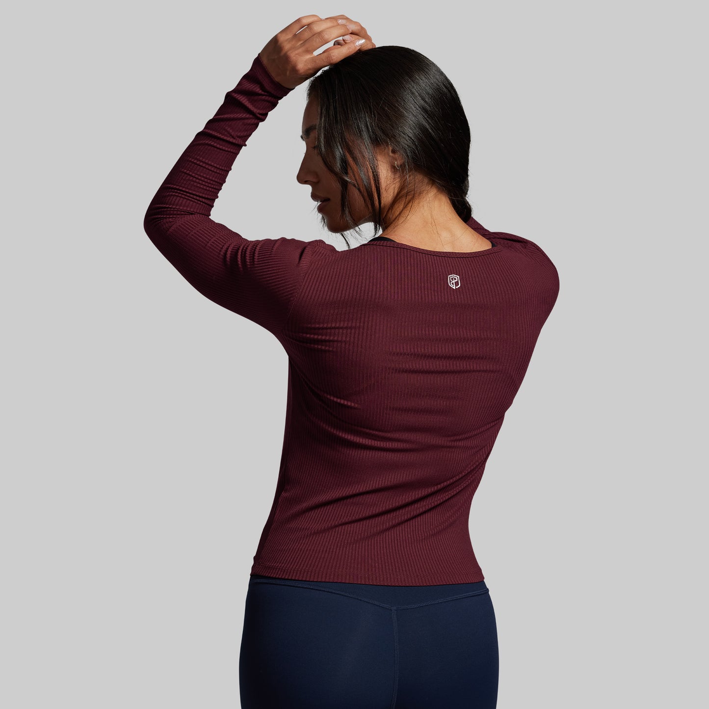 Person wearing a maroon long-sleeve top with a logo on a gray background