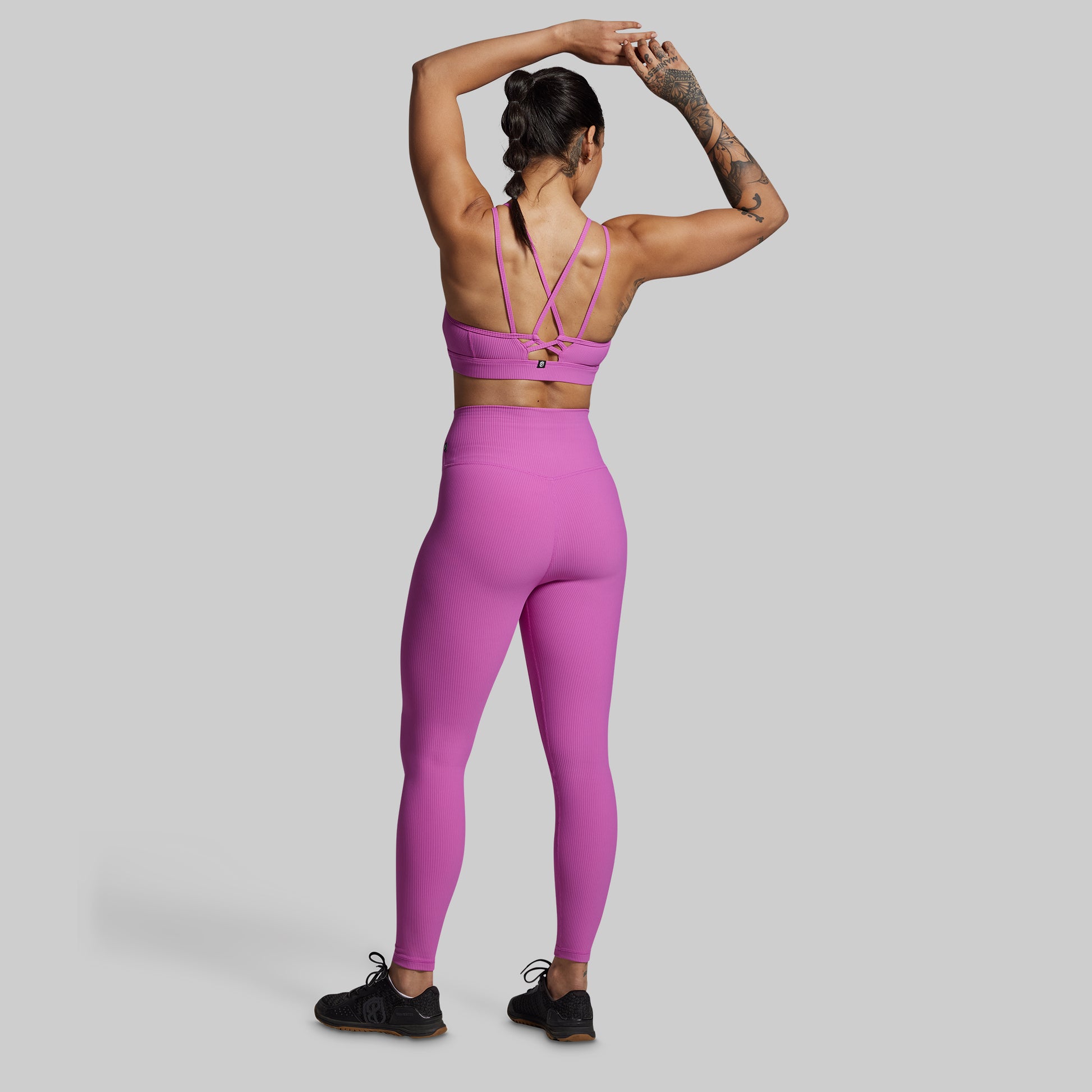 Person wearing a pink sports bra and leggings set on a gray background
