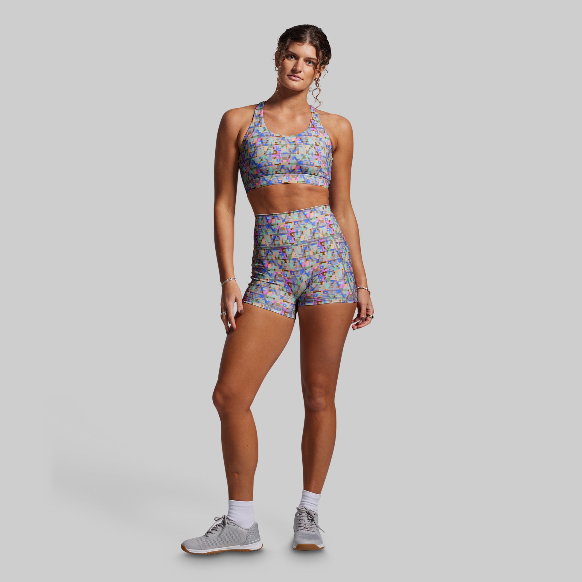 Woman wearing a colorful sports bra and shorts set on a gray background