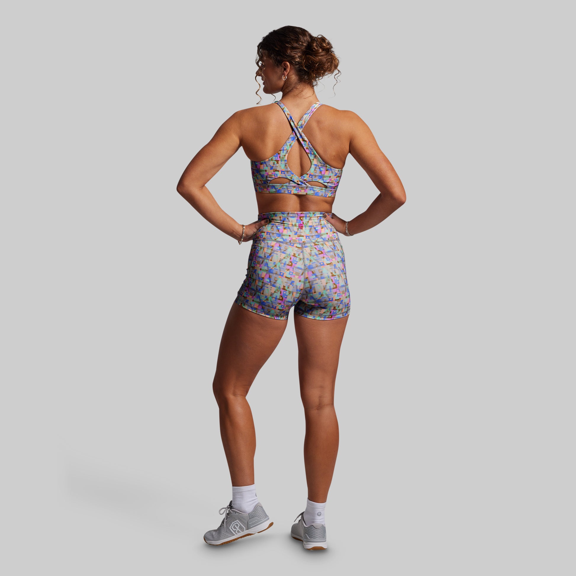Woman wearing a colorful sports bra and shorts set on a gray background