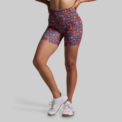 Person wearing colorful patterned shorts and white sneakers on a gray background